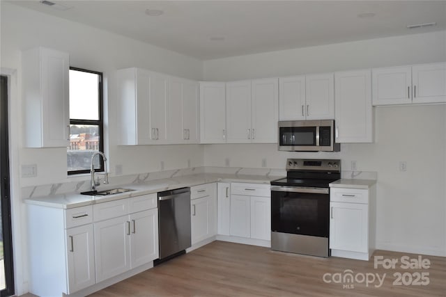 kitchen with appliances with stainless steel finishes, sink, white cabinets, light stone counters, and light wood-type flooring