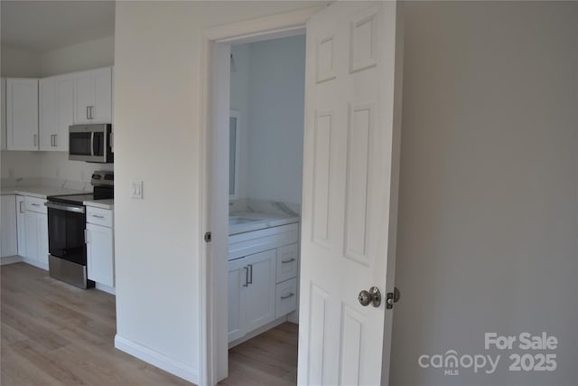 kitchen with stainless steel appliances, white cabinets, and light hardwood / wood-style flooring