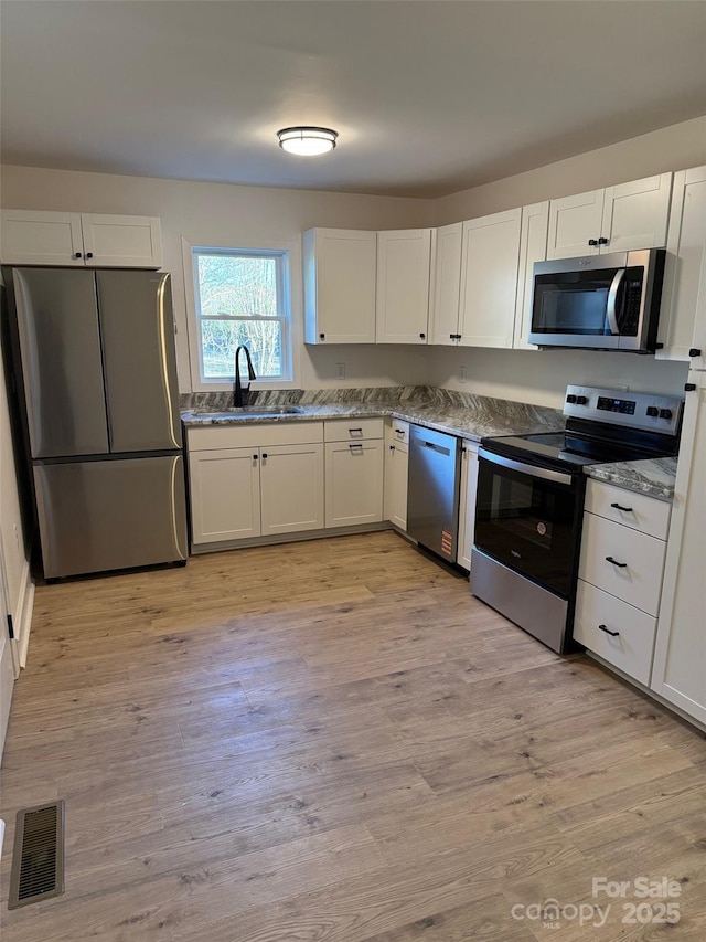 kitchen with sink, appliances with stainless steel finishes, white cabinetry, and light hardwood / wood-style floors