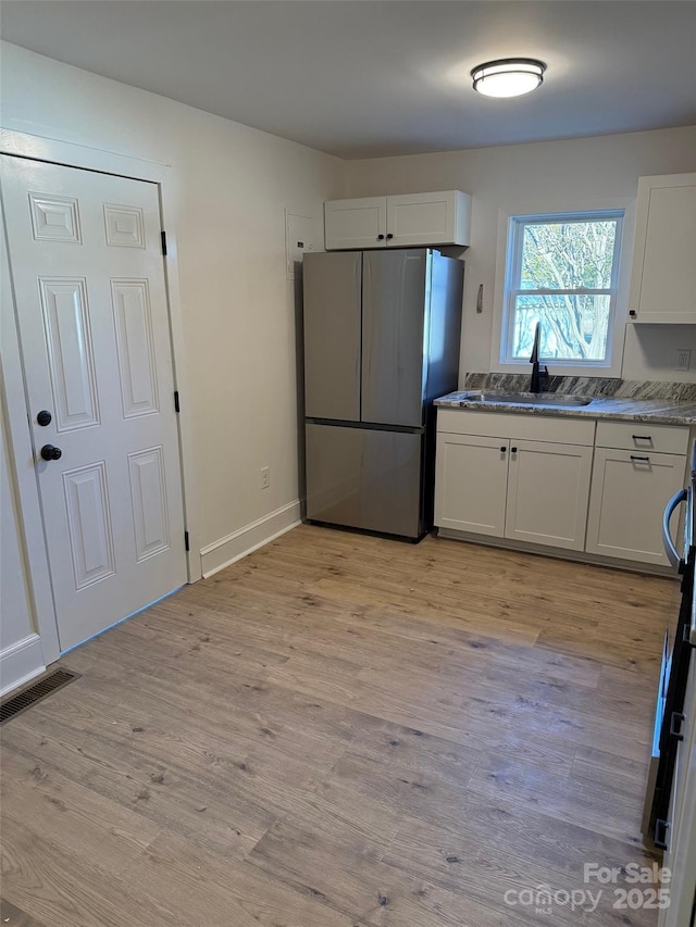 kitchen with sink, stainless steel refrigerator, white cabinets, and light hardwood / wood-style floors