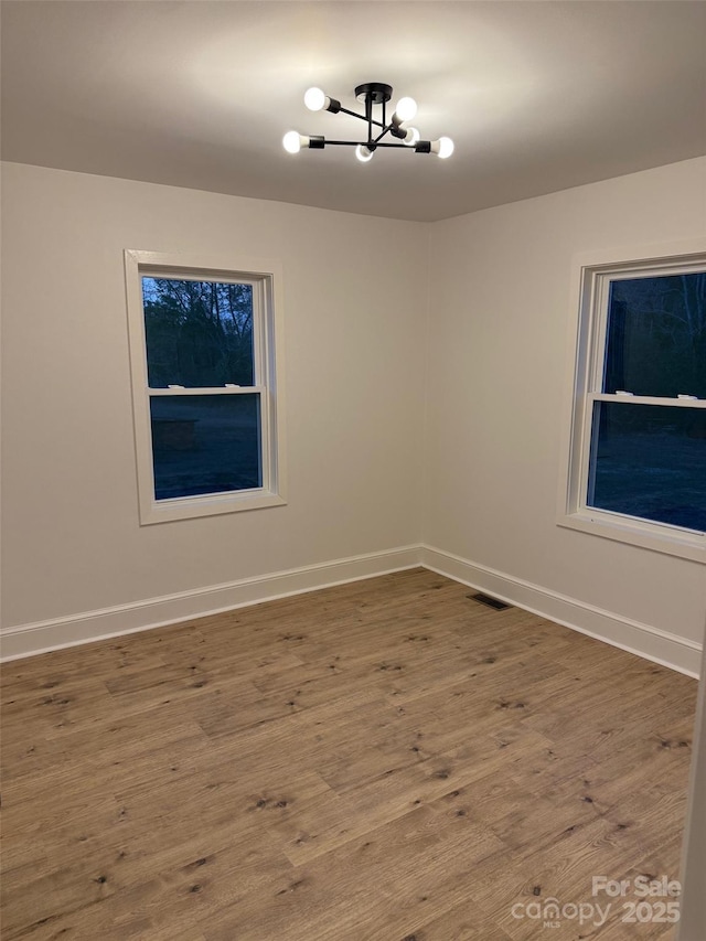 empty room with hardwood / wood-style floors and a notable chandelier