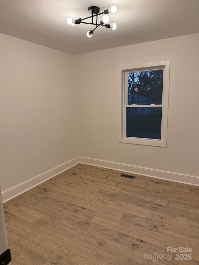 spare room with hardwood / wood-style flooring and a notable chandelier