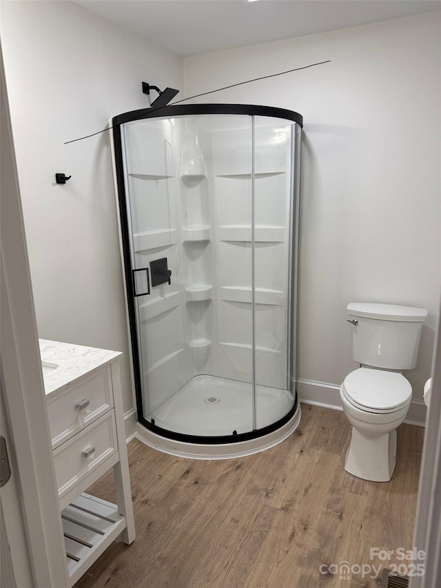 bathroom with toilet, hardwood / wood-style flooring, a shower with shower door, and vanity