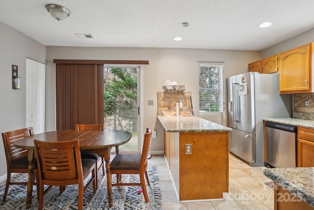 kitchen featuring light stone counters, decorative backsplash, a wealth of natural light, and appliances with stainless steel finishes