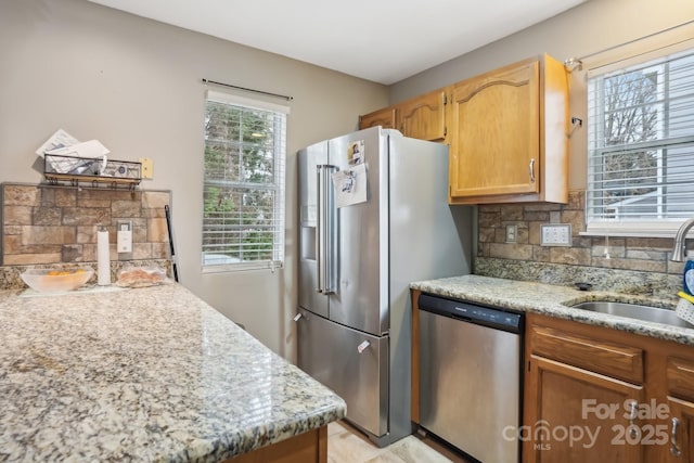 kitchen with appliances with stainless steel finishes, sink, backsplash, and light stone counters