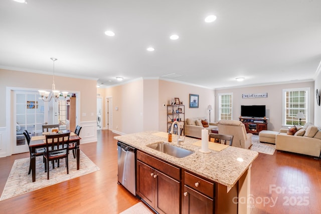 kitchen with sink, decorative light fixtures, a center island with sink, light wood-type flooring, and stainless steel dishwasher