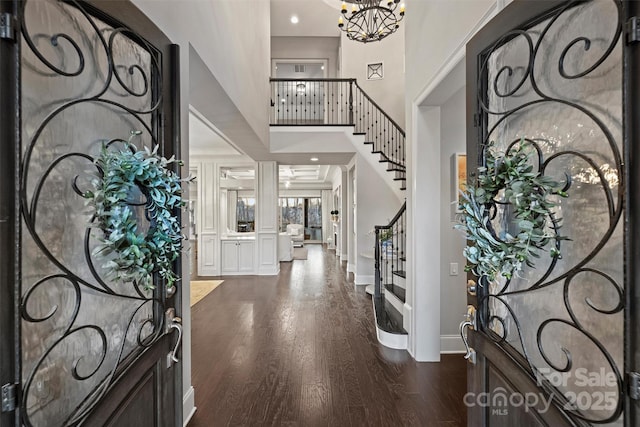 entrance foyer with dark wood-style floors, stairway, a towering ceiling, an inviting chandelier, and baseboards