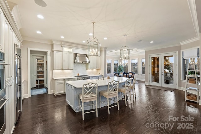 kitchen featuring range hood, a breakfast bar area, white cabinets, hanging light fixtures, and a kitchen island with sink