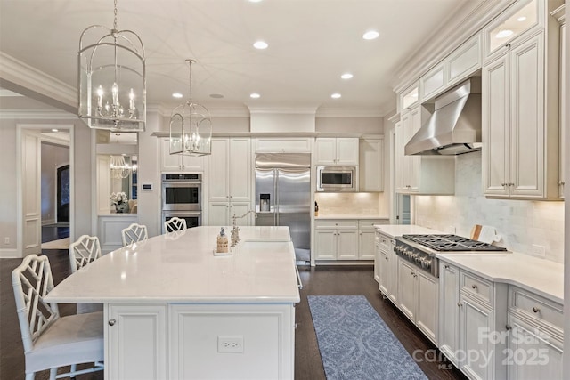 kitchen with built in appliances, an island with sink, a breakfast bar area, and wall chimney range hood