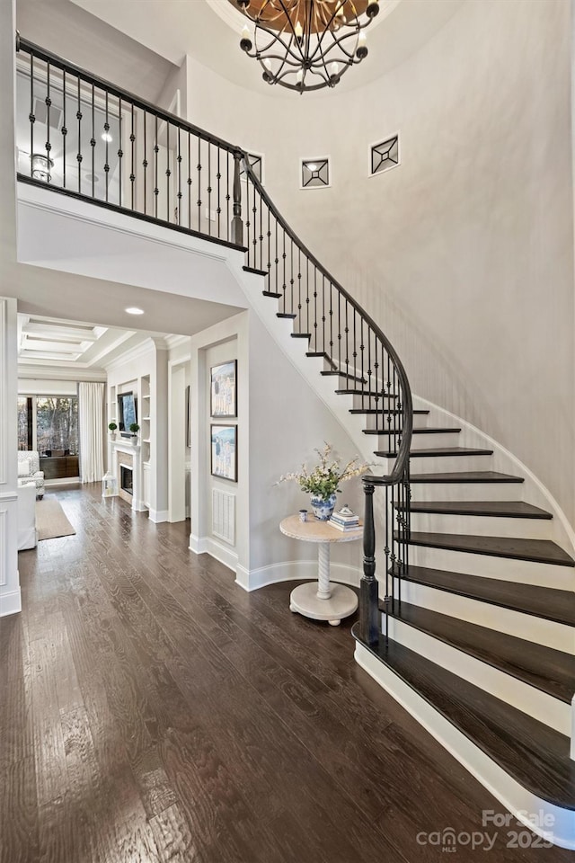 stairway featuring a fireplace, a high ceiling, an inviting chandelier, wood finished floors, and baseboards