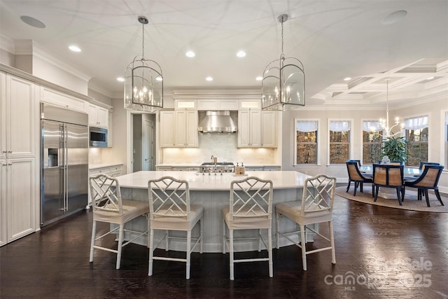 kitchen with built in appliances, light countertops, wall chimney range hood, and an inviting chandelier