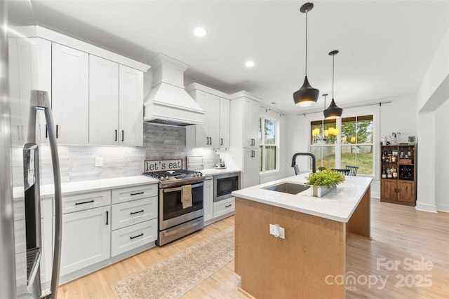 kitchen with white cabinetry, an island with sink, stainless steel appliances, premium range hood, and sink