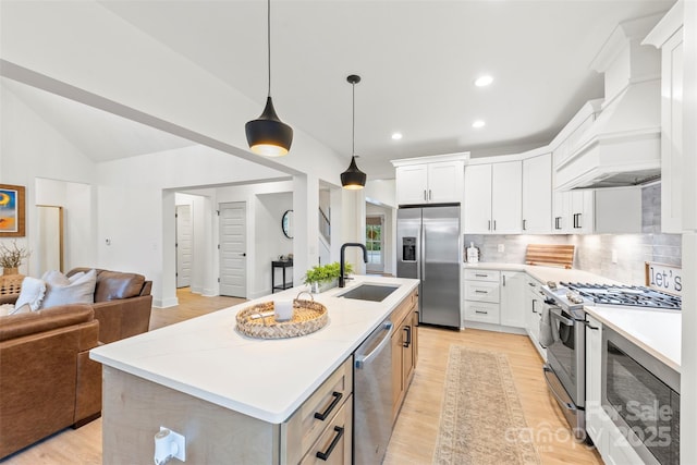 kitchen with appliances with stainless steel finishes, a center island with sink, premium range hood, white cabinets, and pendant lighting