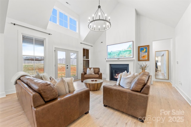 living room featuring a notable chandelier, high vaulted ceiling, french doors, and light hardwood / wood-style flooring