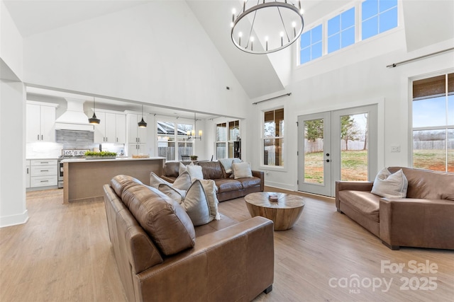 living room with light wood-type flooring, an inviting chandelier, french doors, and a healthy amount of sunlight