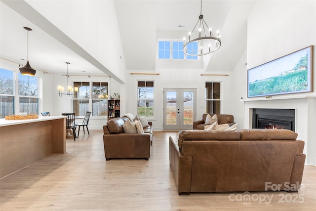 living room featuring a notable chandelier, light hardwood / wood-style flooring, french doors, and a towering ceiling