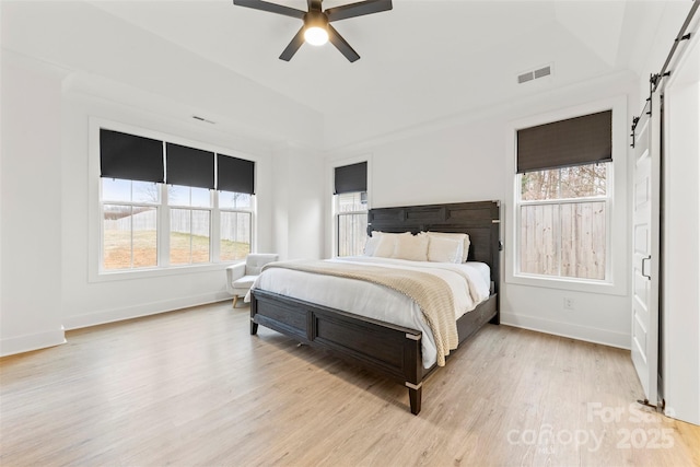 bedroom with light wood-type flooring, ceiling fan, and a barn door