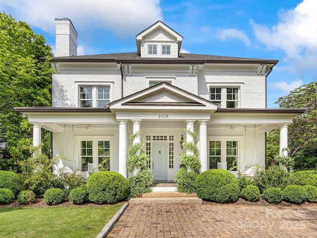 colonial inspired home featuring covered porch, a chimney, and brick siding