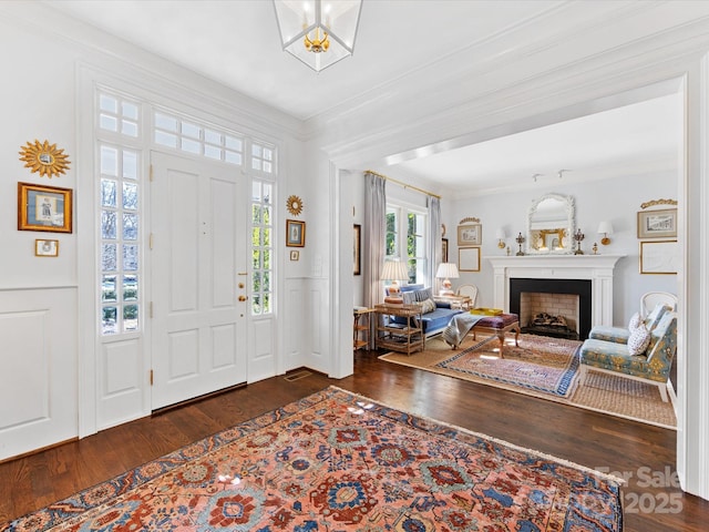 foyer entrance featuring ornamental molding, a decorative wall, wood finished floors, and a fireplace