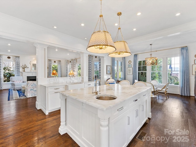 kitchen with light stone countertops, a sink, white cabinetry, a large island, and dark wood-style floors