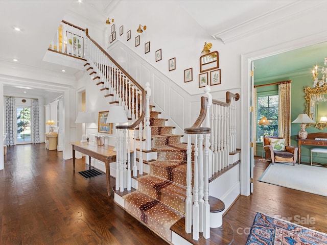 staircase featuring crown molding, a high ceiling, wood finished floors, and a notable chandelier