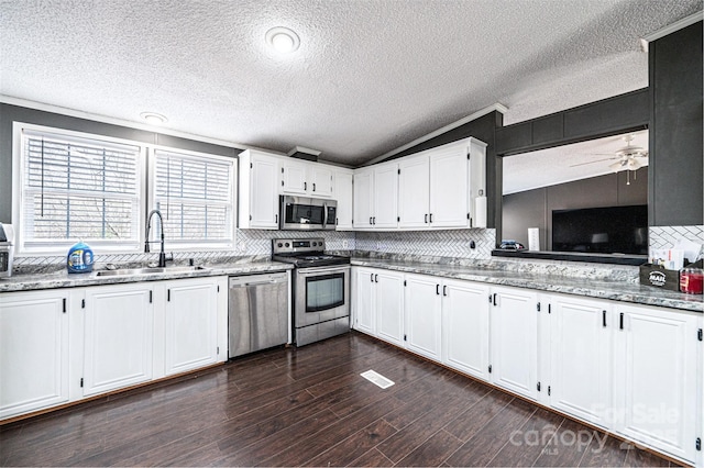 kitchen with lofted ceiling, sink, white cabinetry, appliances with stainless steel finishes, and light stone countertops