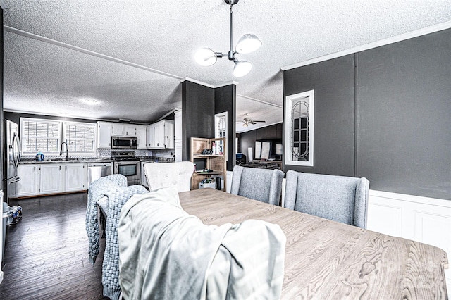 dining space with sink, crown molding, dark hardwood / wood-style flooring, ceiling fan with notable chandelier, and vaulted ceiling