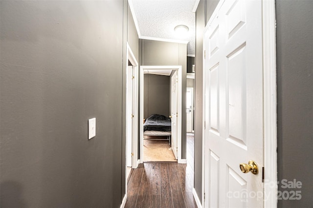 corridor with dark wood-type flooring, ornamental molding, and a textured ceiling