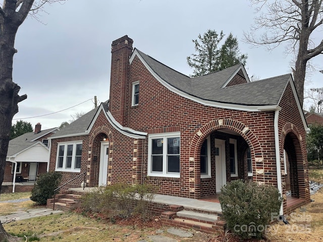 view of front of house with a shingled roof, brick siding, and a chimney