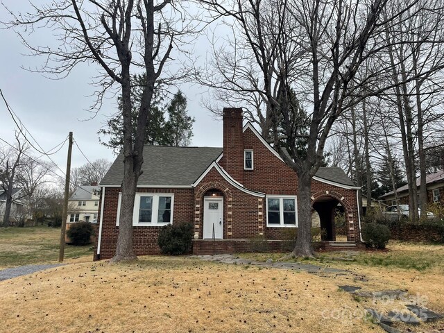 view of front of house with brick siding, a chimney, a front yard, and roof with shingles