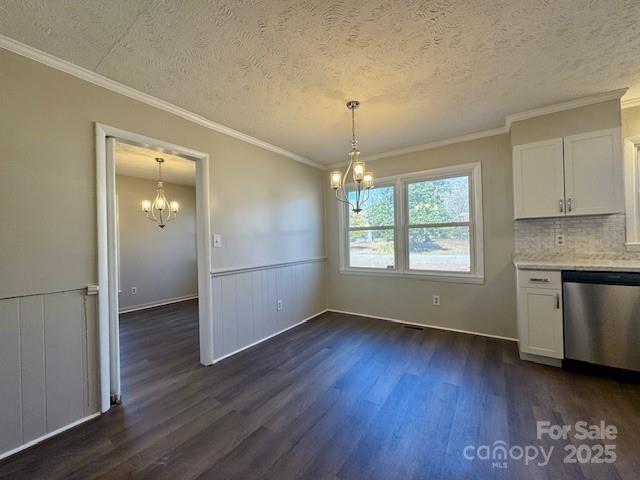 unfurnished dining area with a notable chandelier, a textured ceiling, dark wood-type flooring, and ornamental molding