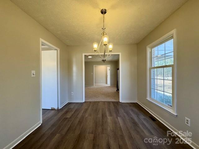 unfurnished dining area with a textured ceiling, a notable chandelier, and dark hardwood / wood-style flooring