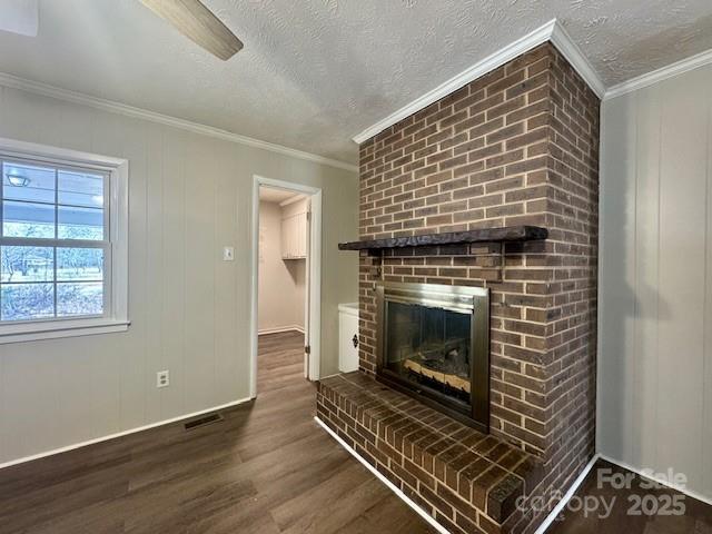 unfurnished living room with a fireplace, dark wood-type flooring, crown molding, and a textured ceiling