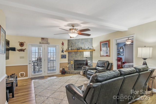 living room featuring hardwood / wood-style flooring, ceiling fan, a stone fireplace, and beam ceiling