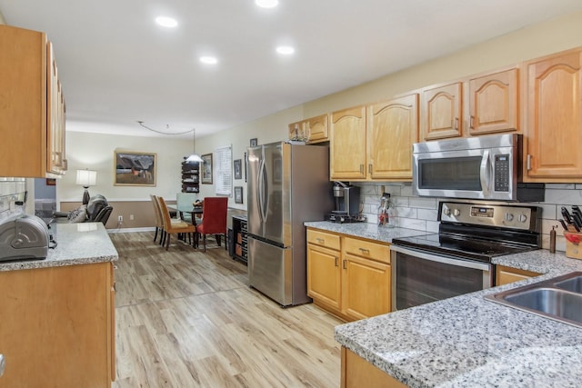 kitchen featuring sink, appliances with stainless steel finishes, light stone counters, decorative backsplash, and light wood-type flooring