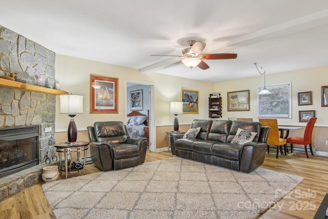 living room featuring a stone fireplace, ceiling fan, and light wood-type flooring