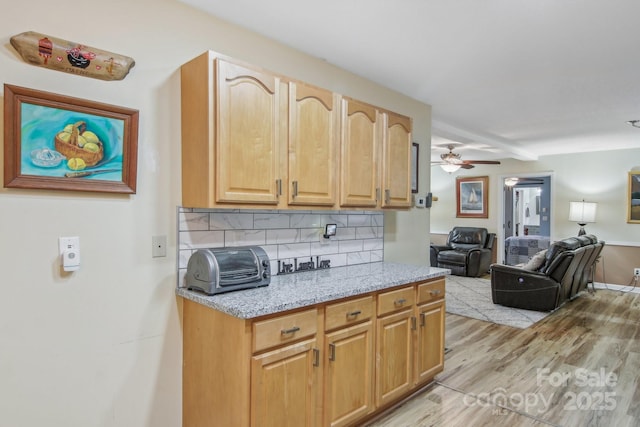 kitchen with tasteful backsplash, light stone counters, light hardwood / wood-style flooring, and ceiling fan