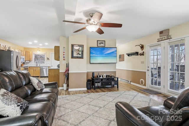 living room with ceiling fan, a baseboard radiator, sink, and light hardwood / wood-style floors