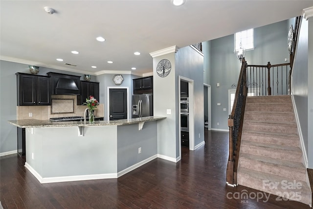 kitchen featuring dark cabinets, dark wood-type flooring, light stone countertops, stainless steel appliances, and backsplash