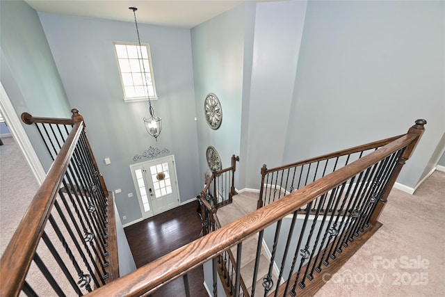 stairs with a chandelier, a towering ceiling, baseboards, and wood finished floors