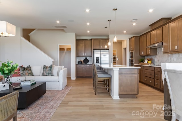 kitchen featuring a breakfast bar area, hanging light fixtures, backsplash, stainless steel appliances, and an island with sink