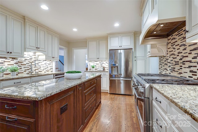 kitchen featuring premium range hood, high quality appliances, sink, and light stone counters