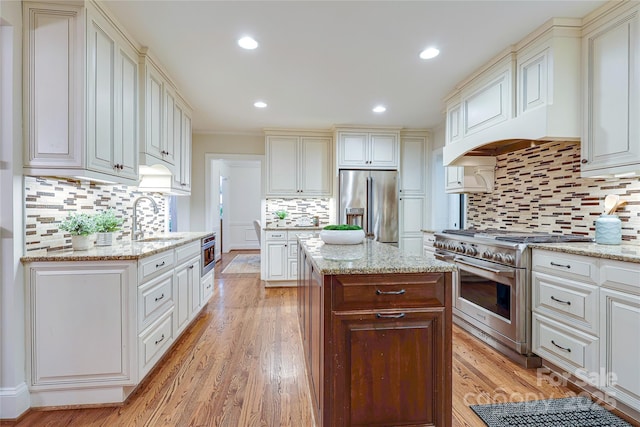 kitchen featuring sink, high end appliances, light stone countertops, light hardwood / wood-style floors, and a kitchen island