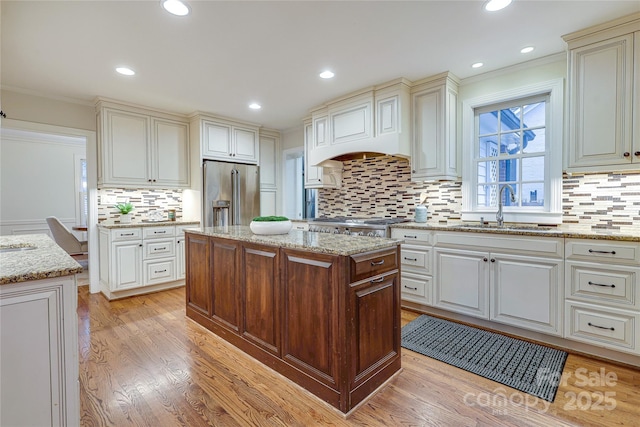 kitchen with a center island, high end fridge, sink, and light stone counters