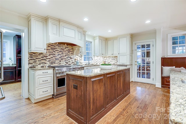 kitchen featuring high end stainless steel range oven, a center island, light stone counters, and light hardwood / wood-style floors