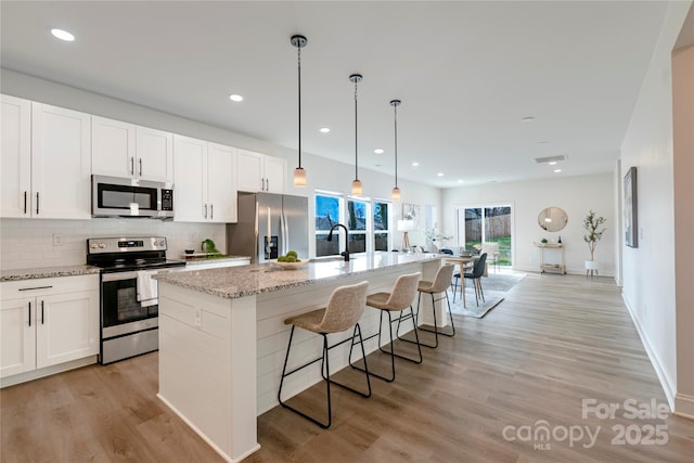 kitchen with appliances with stainless steel finishes, a breakfast bar, white cabinetry, an island with sink, and hanging light fixtures