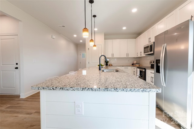 kitchen with decorative light fixtures, sink, white cabinets, a kitchen island with sink, and stainless steel appliances