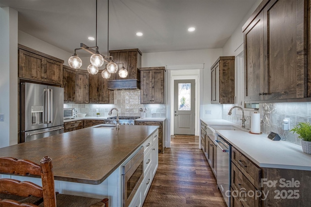 kitchen featuring pendant lighting, tasteful backsplash, an island with sink, stainless steel appliances, and dark wood-type flooring