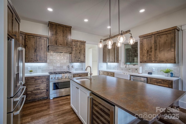 kitchen with sink, premium range hood, high end appliances, wine cooler, and a center island with sink