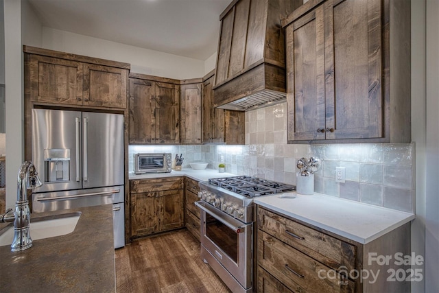 kitchen with dark wood-type flooring, sink, high end appliances, custom range hood, and decorative backsplash